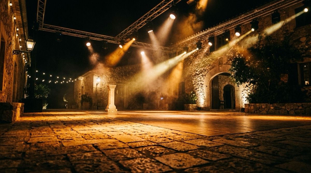 An outdoor finca dance floor washed in amber by LED fixtures, with moving heads above and haze cutting through the beams